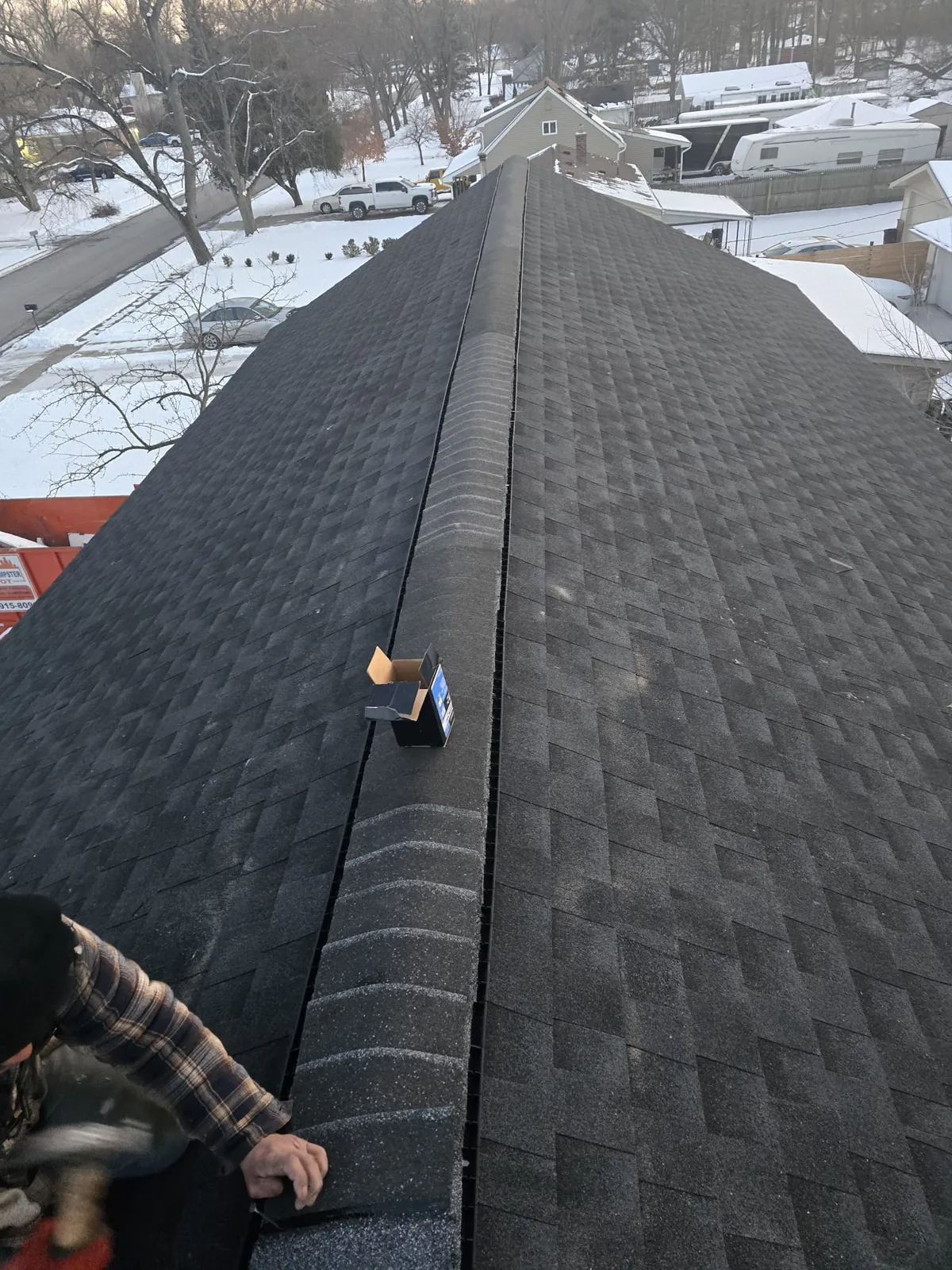 Roofer installing architectural shingles at the ridge of a steep roof, Mid-Michigan